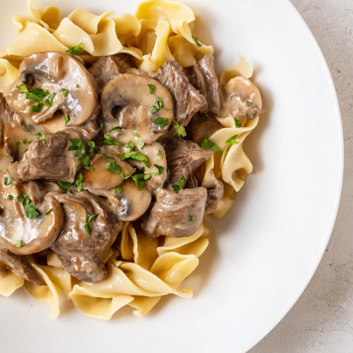 Comforting Beef Stroganoff over fluffy egg noodles is garnished with fresh parsley, served hot in a rustic skillet for a family dinner.  