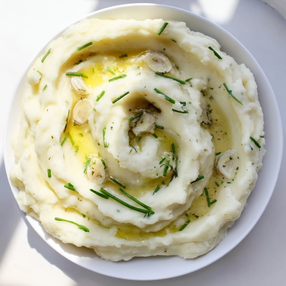 Steaming Garlic Mashed Potatoes with Roasted Garlic are served alongside a slice of buttery bread, perfect for a comforting side dish.