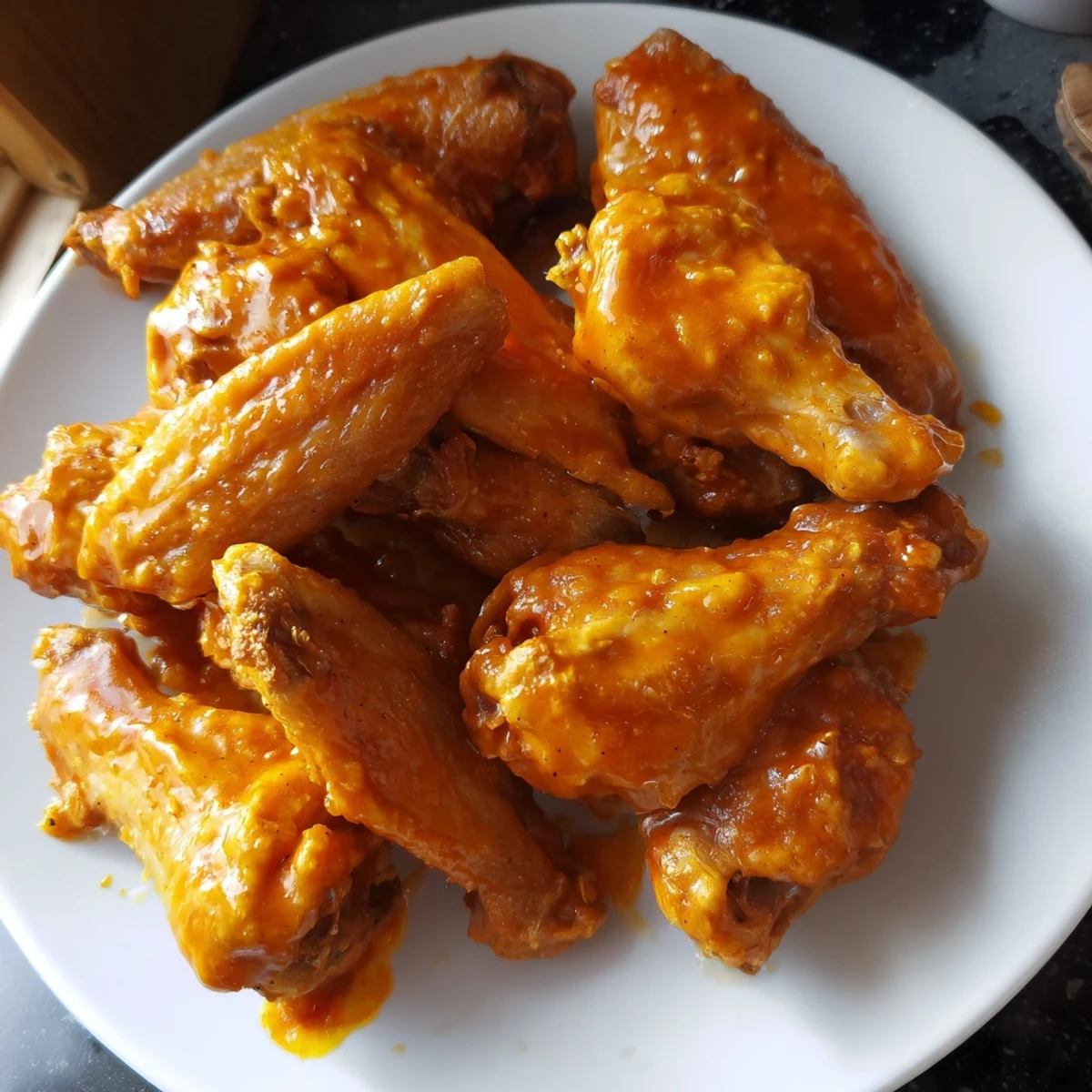 Buffalo sauce glazed chicken wings in a bowl, served with crunchy celery and carrot sticks for a game day snack.