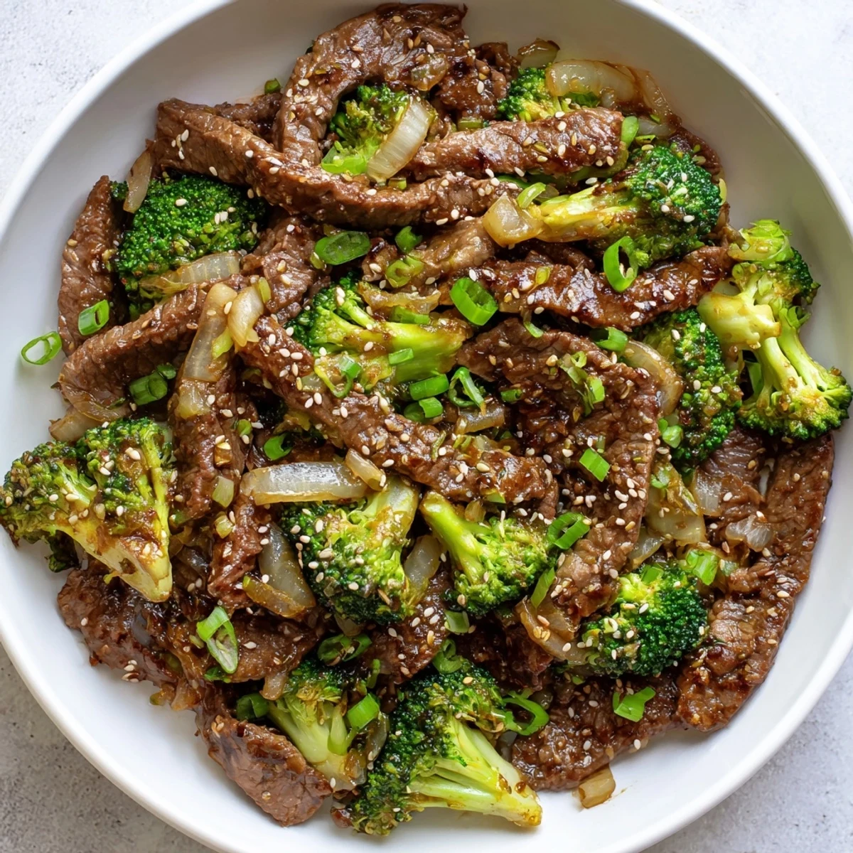 Close-up shows seared beef and broccoli tossed in a dark, glossy Beef and Broccoli Stir Fry with Garlic Sauce, garnished with scallions and sesame seeds for crunch.