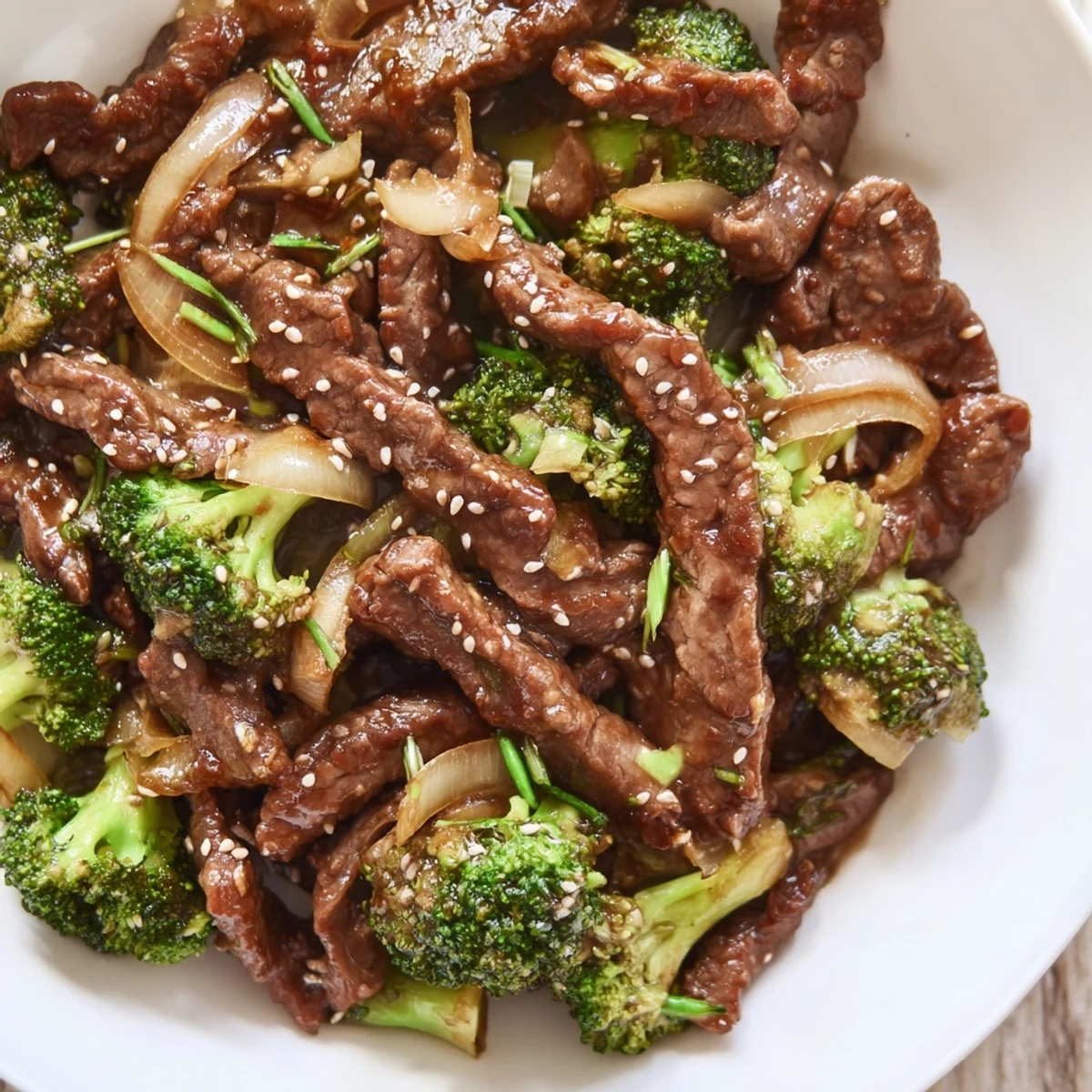 A fork lifts saucy Beef and Broccoli Stir Fry with Garlic Sauce, with onions and sesame seeds, ideal for a fast weeknight dinner served over noodles.