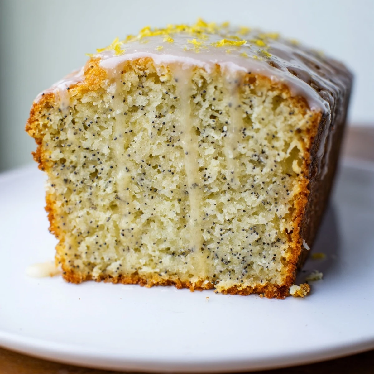 Freshly glazed Lemon Poppy Seed Loaf Cake on a white plate with lemon slices and blueberries for garnish.