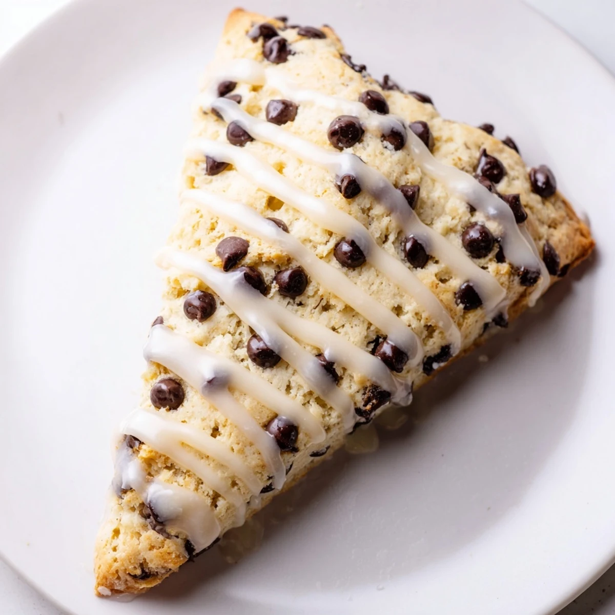 Freshly baked Chocolate Chip Scones with Vanilla Glaze served beside a steaming cup of black tea.