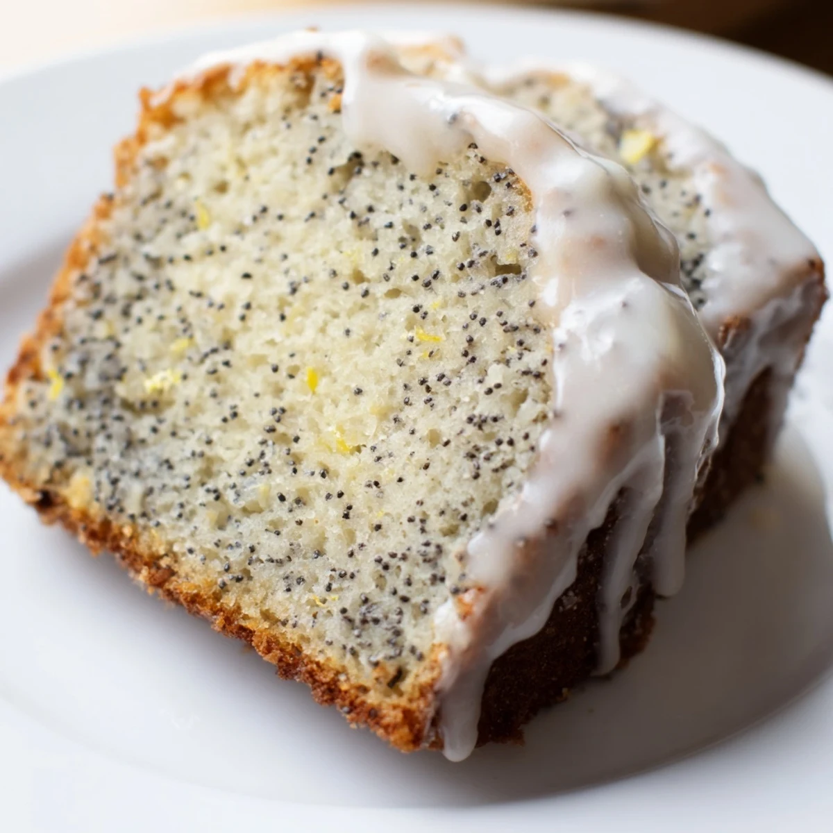 Slices of moist Lemon Poppy Seed Loaf show poppy seeds and lemon zest with tea.