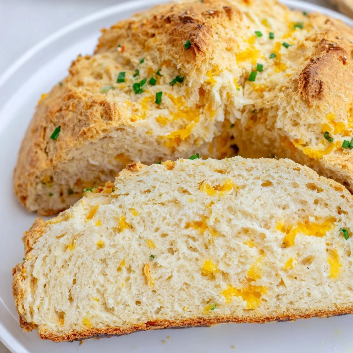 A close-up of Savory Cheddar & Chive Irish Soda Bread with a golden, crackly crust, melted cheddar, and green chive flecks.