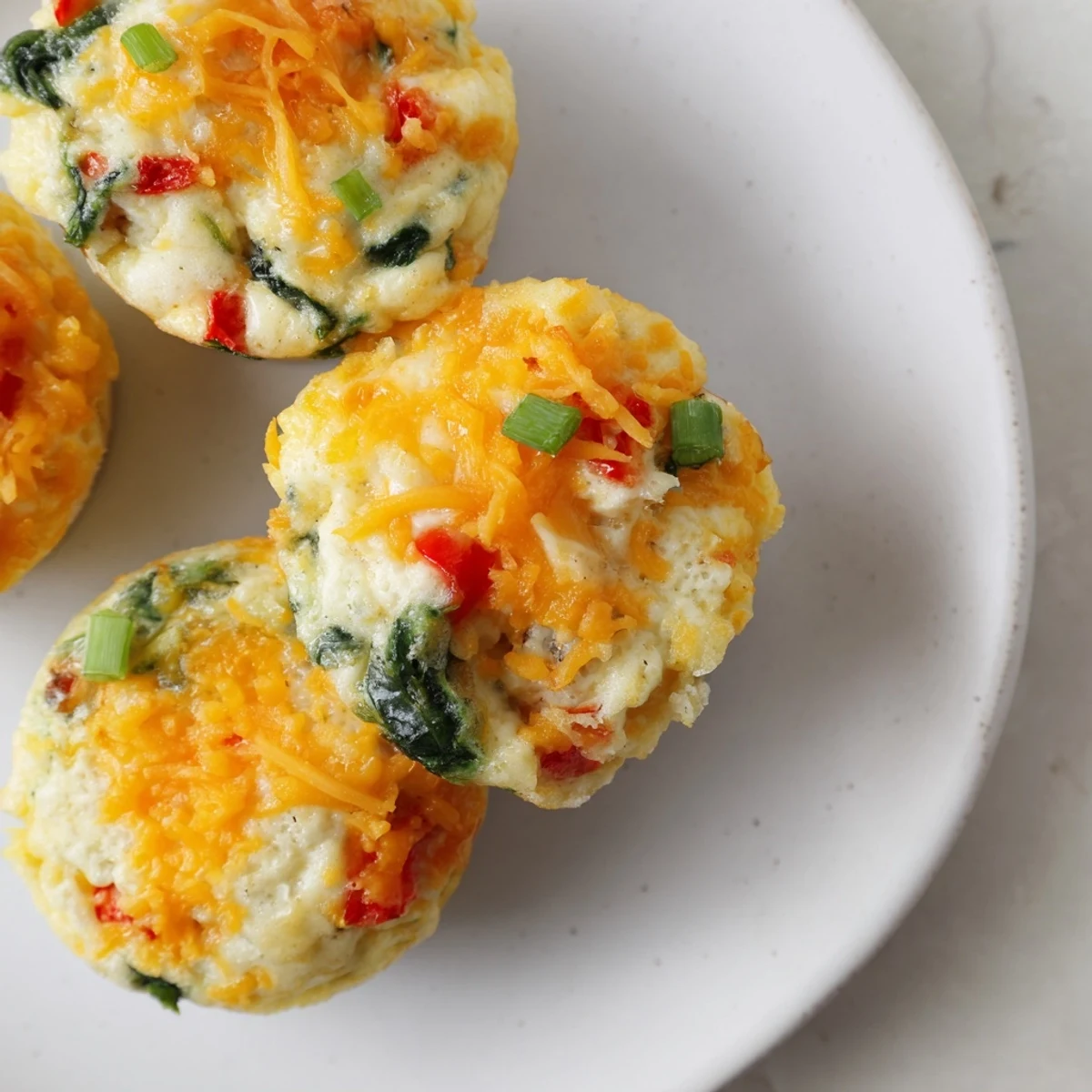 Golden-brown Cottage Cheese Egg Bites fresh from the muffin tin, speckled with green spinach and red bell pepper.