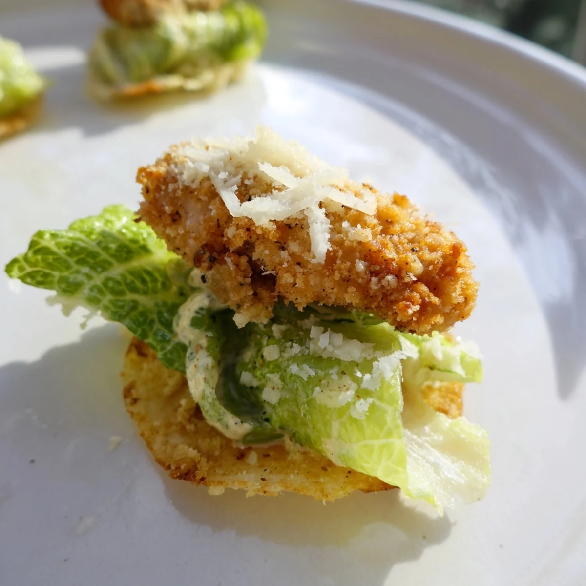 A close-up of Crispy Chicken Caesar Salad Chips showing crunchy chicken bites on seasoned potato chips drizzled with creamy Caesar dressing.