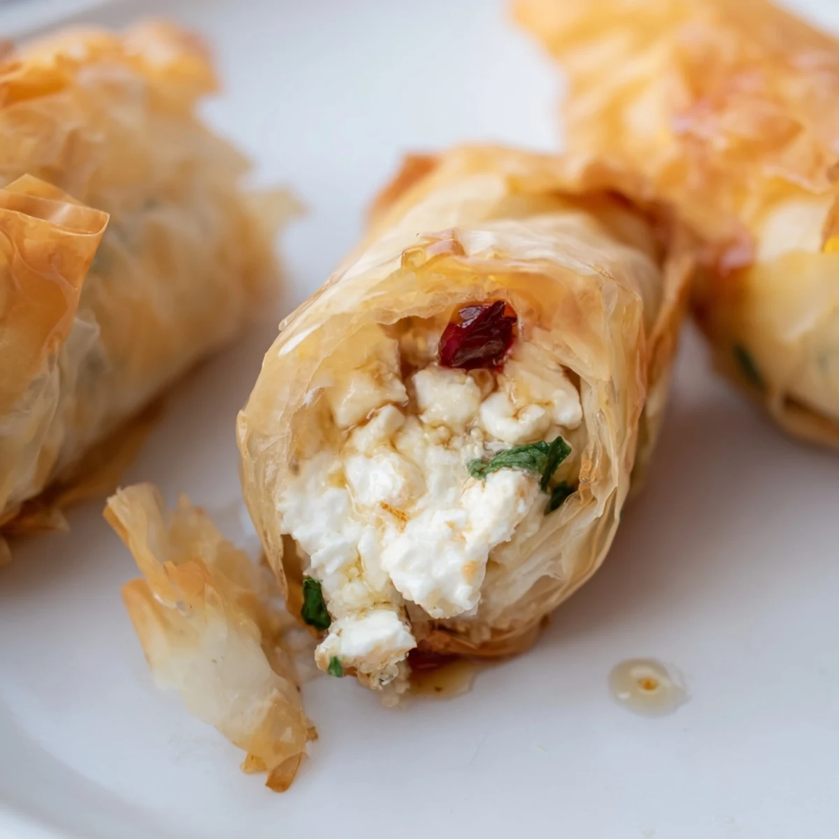 A close-up of golden, crispy Oven Fried Feta Rolls with Chili Honey on a wooden platter, garnished with fresh dill. 