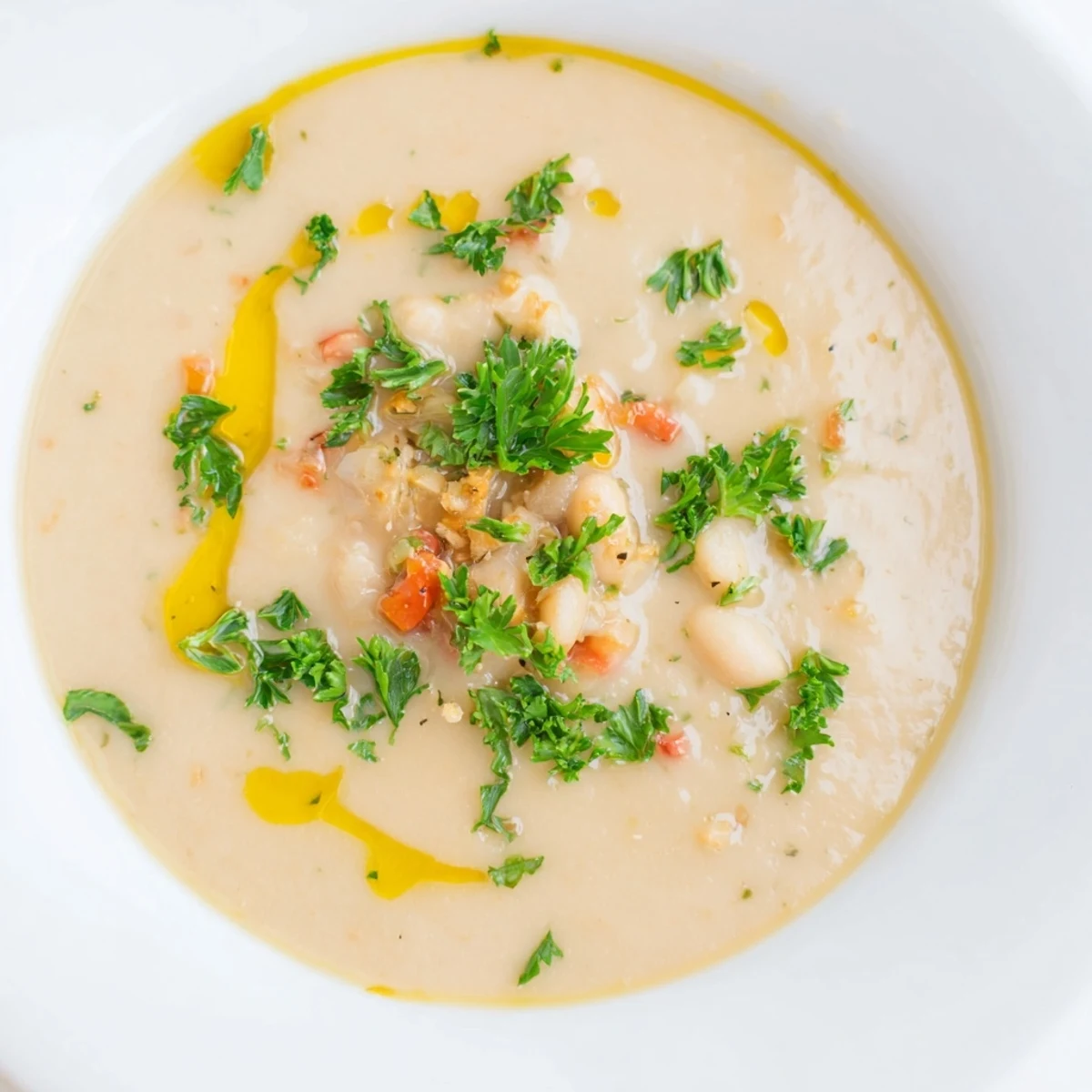A spoon dips into the creamy Rosemary and Roasted Garlic White Bean Soup garnished with a drizzle of olive oil.