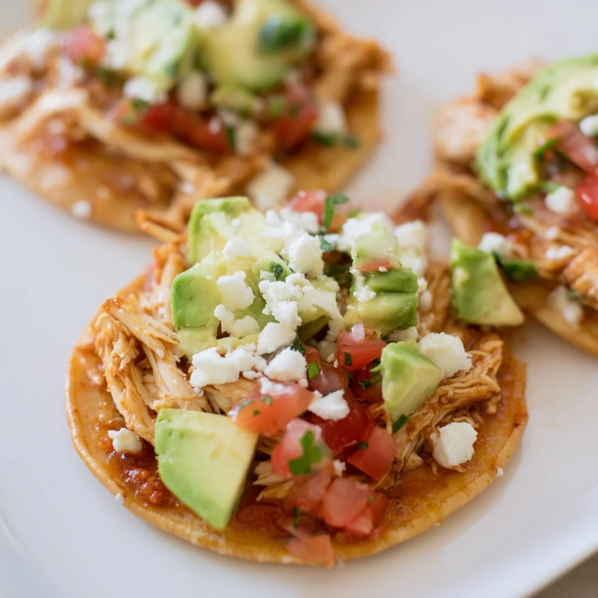 Golden-brown crispy mini chicken tostadas topped with fresh pico de gallo and diced avocado.