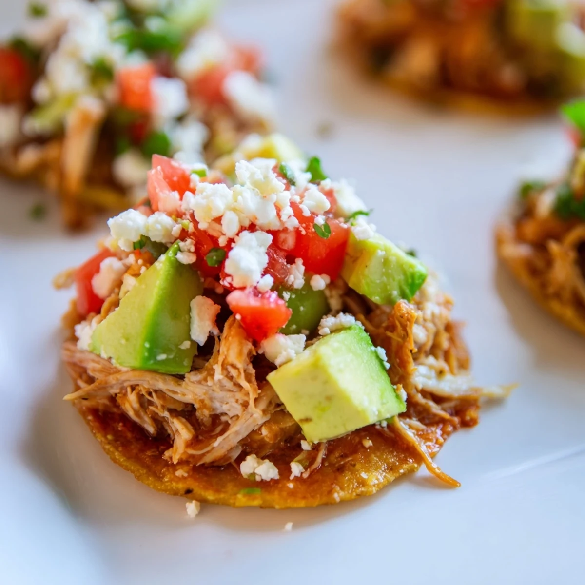 Party-ready mini chicken tostadas garnished with cheese and lime wedges on a rustic platter.