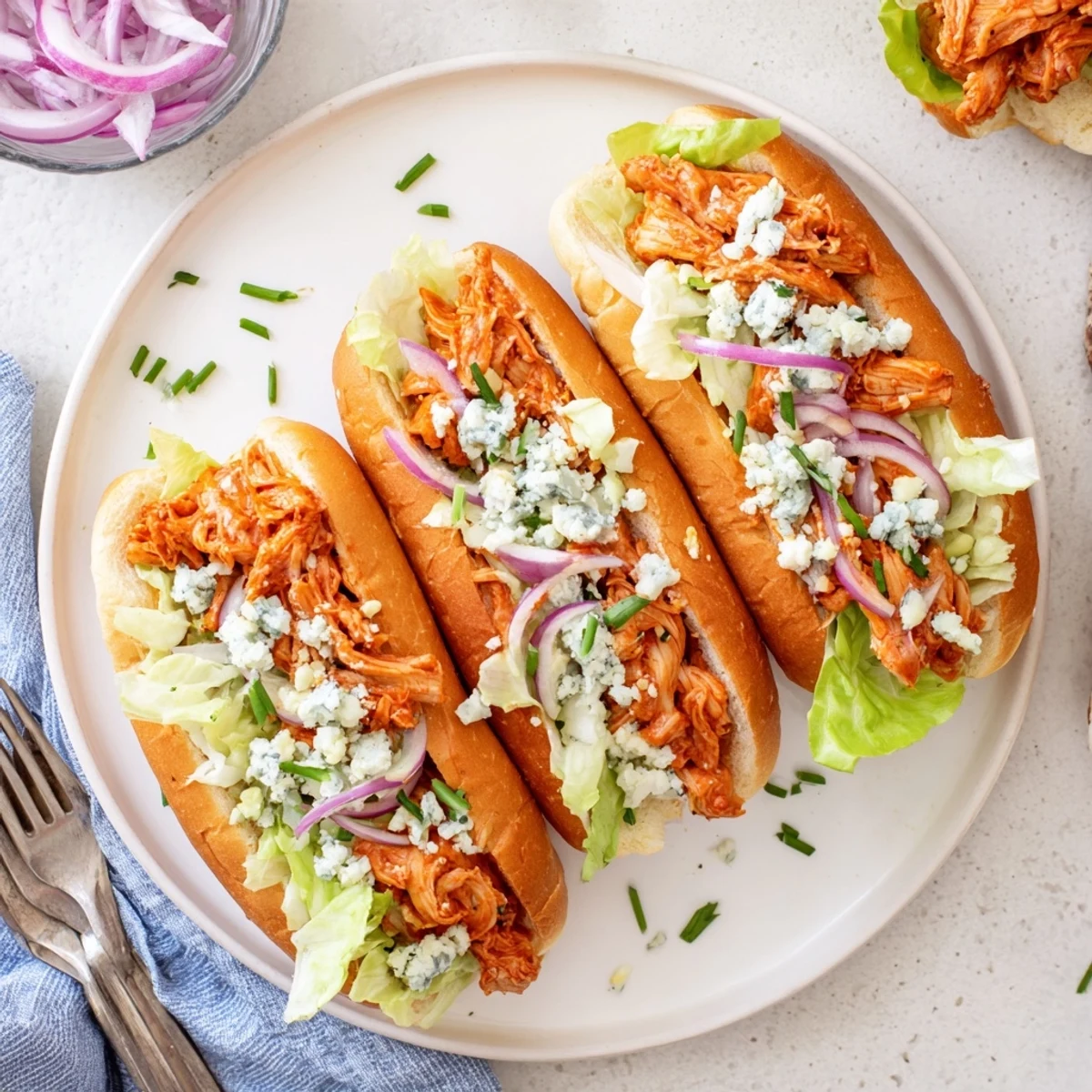 Vibrant spicy Buffalo chicken sliders featuring tender shredded chicken drenched in tangy sauce, creamy blue cheese crumbles, crisp lettuce, and soft toasted buns on a platter.