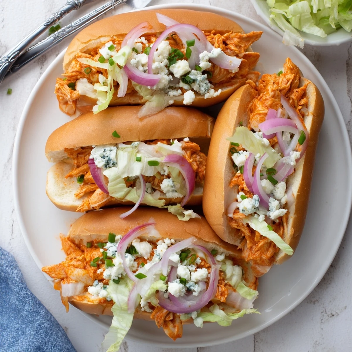 Freshly baked spicy Buffalo chicken sliders garnished with red onion and chives, showcasing melted blue cheese and shredded lettuce tucked inside golden slider buns.