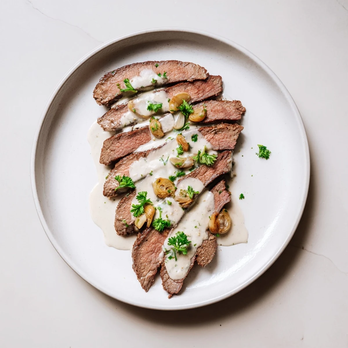 A perfectly seared Flank Steak With Roasted Garlic Sauce sliced thinly and drizzled with velvety sauce.