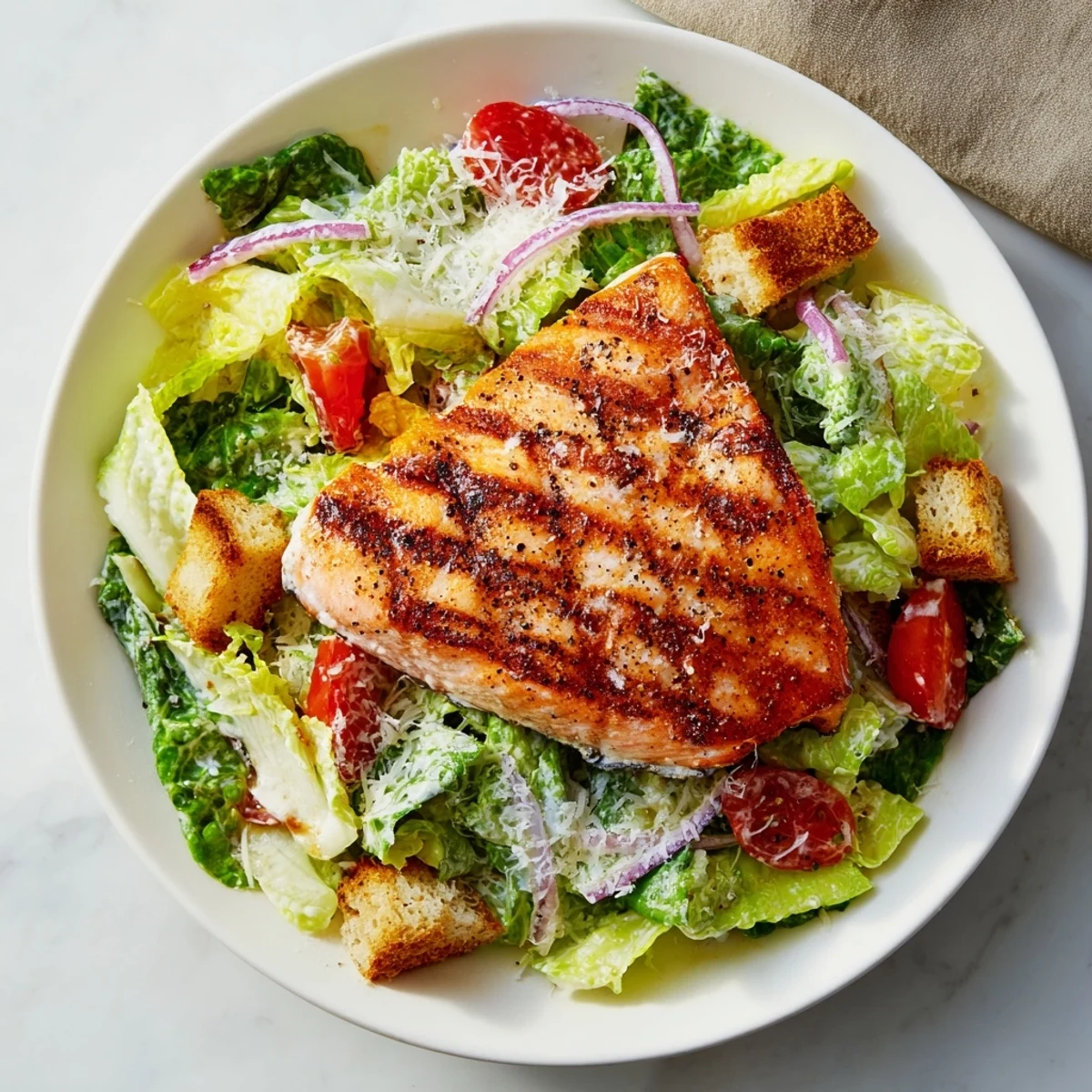 Golden charred salmon atop a vibrant Caesar salad with cherry tomatoes, red onion, and creamy Parmesan dressing