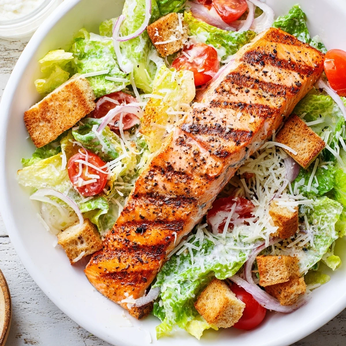 Fresh grilled salmon fillet resting over crisp romaine lettuce with tangy Caesar dressing and golden croutons