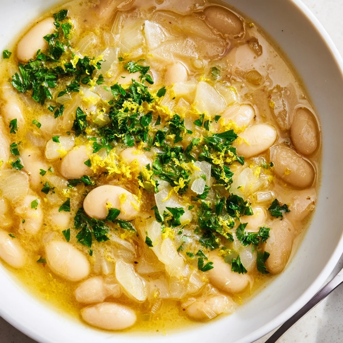 Creamy white beans in golden miso butter broth garnished with fresh green herbs and lemon zest