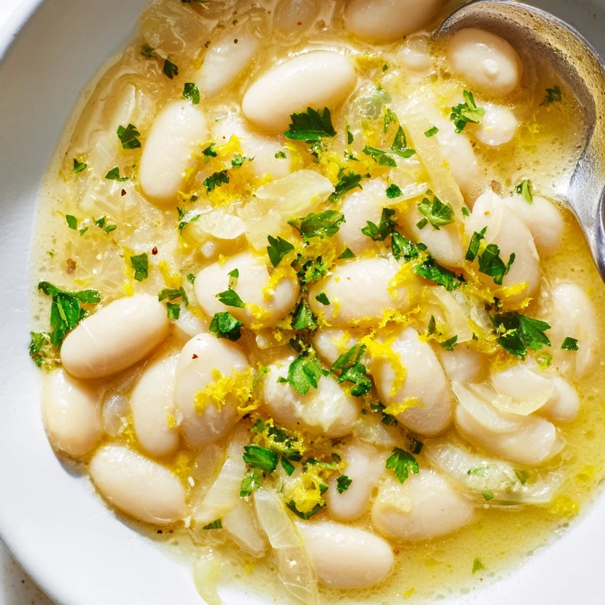 Spoon lifting tender white beans from rich miso-infused butter broth with fresh herb garnish