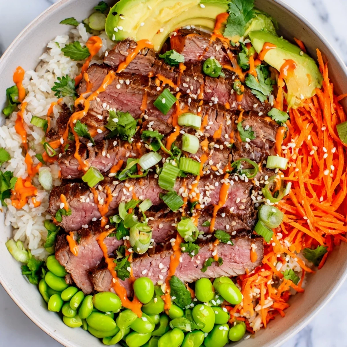 Protein-packed flank steak bowl featuring marinated grilled beef, crunchy edamame and carrots, creamy avocado slices, and zesty sauce