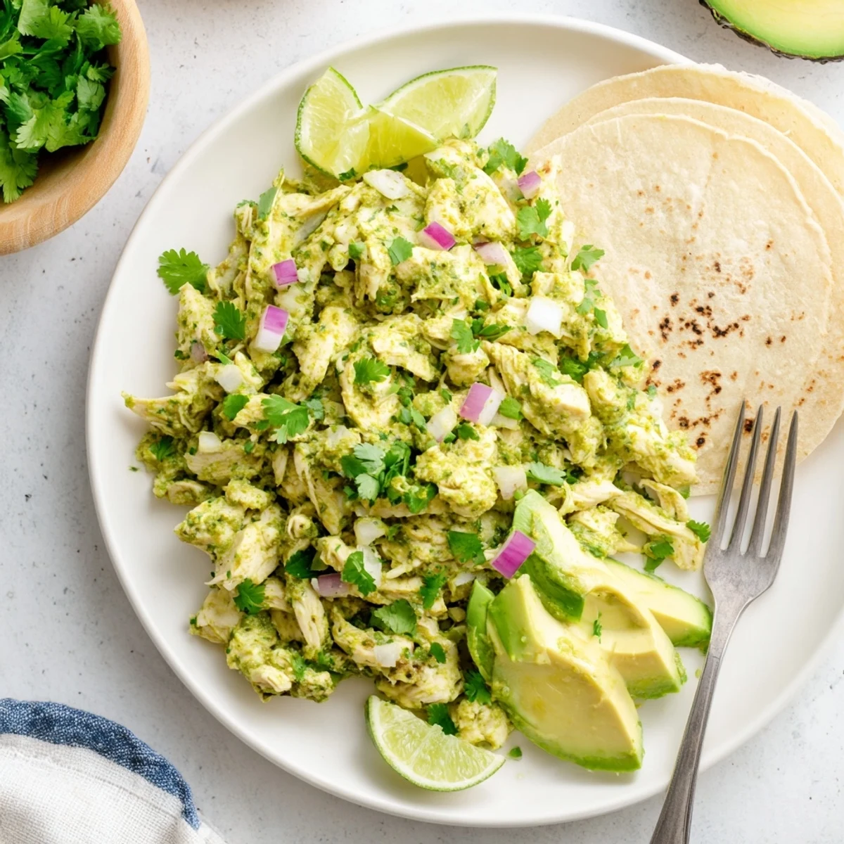 Salsa verde chicken simmered in zesty green sauce, garnished with fresh cilantro and lime