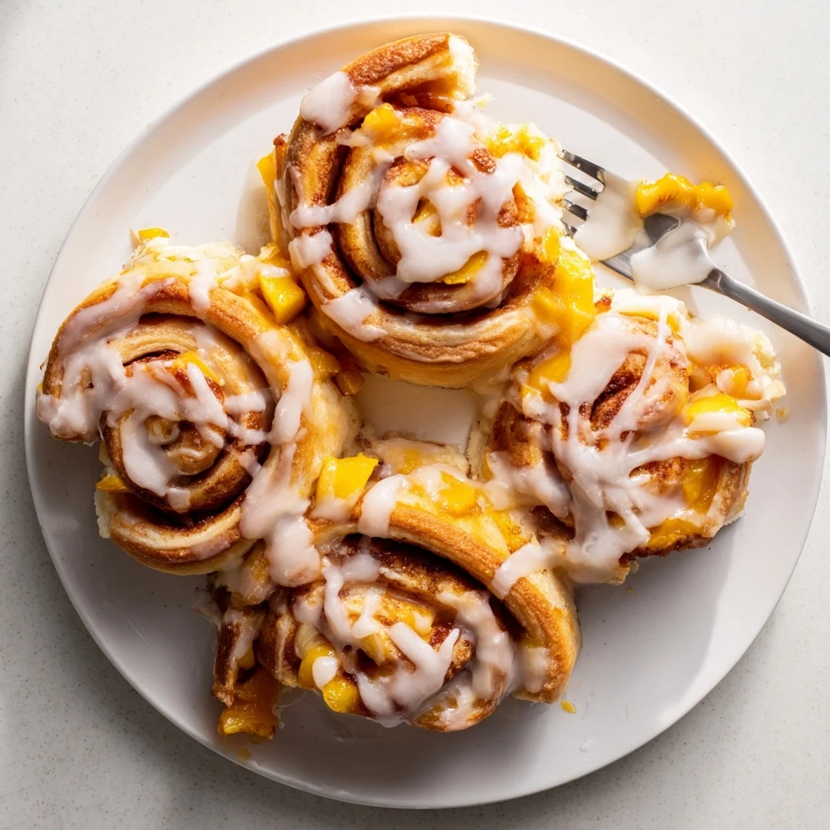 Golden peach pie cinnamon rolls dripping with vanilla glaze on a serving platter