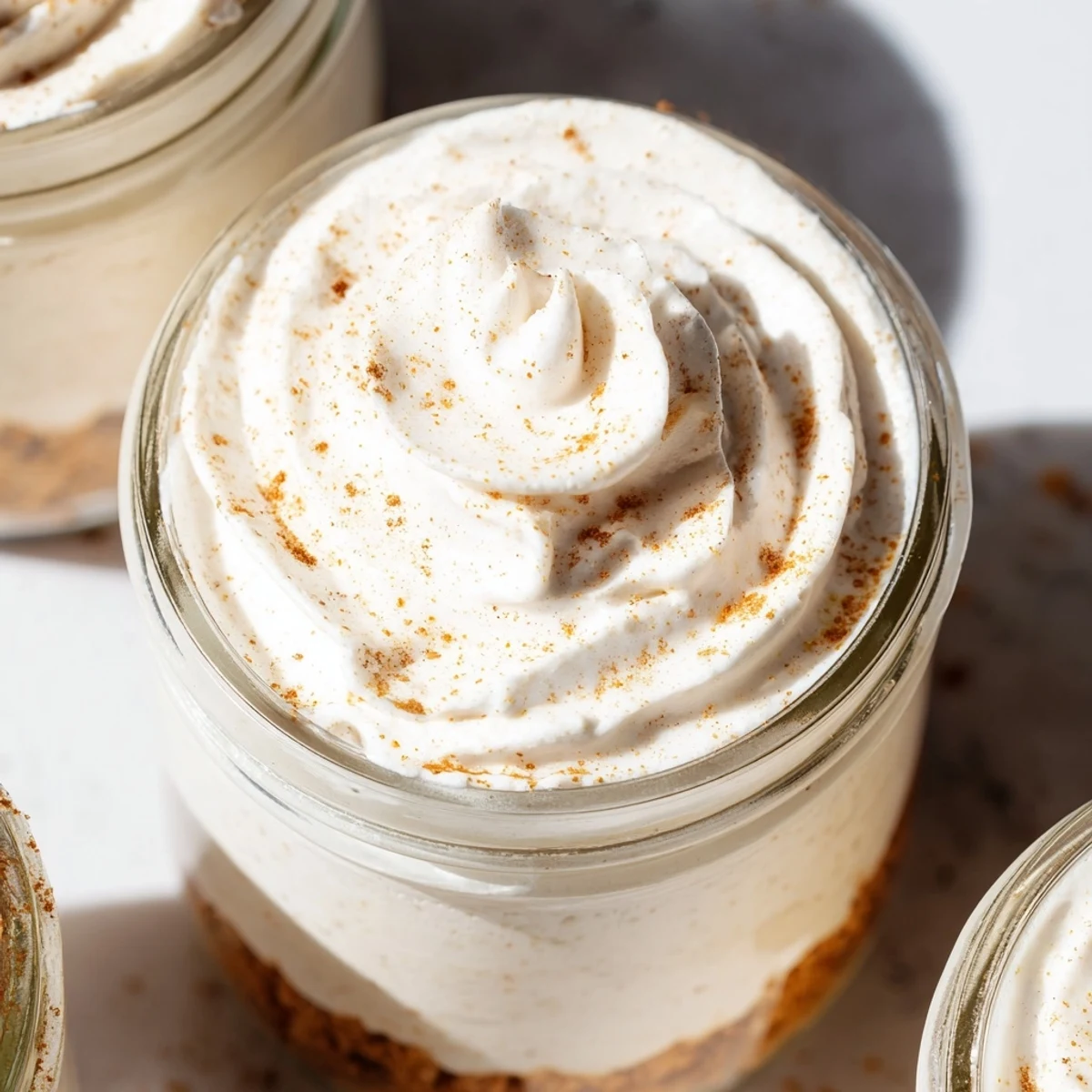 Portable mason jar desserts featuring smooth spiced cheesecake over golden crust finished with sweet cinnamon sprinkle