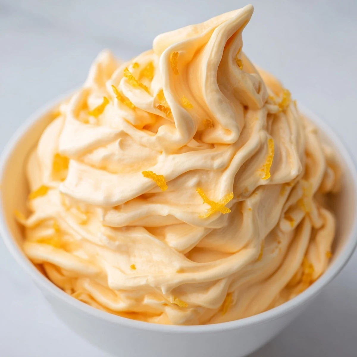 Creamy homemade orange Dole Whip swirled into a tall glass with fresh orange zest sprinkled on top
