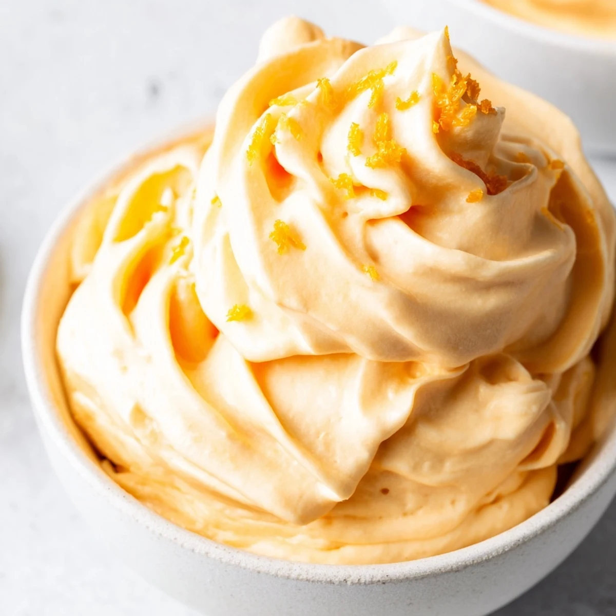 Vibrant homemade orange Dole Whip piped into a swirl garnished with orange zest against a bright background