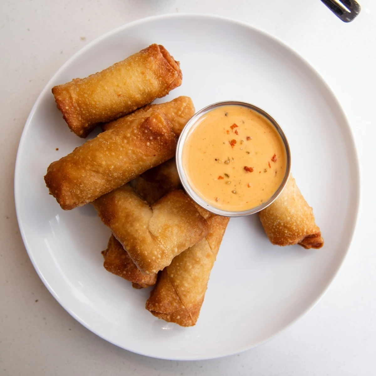 Plate of fried Voodoo Egg rolls showcasing their golden crunch alongside a creamy homemade spicy dipping sauce for appetizers