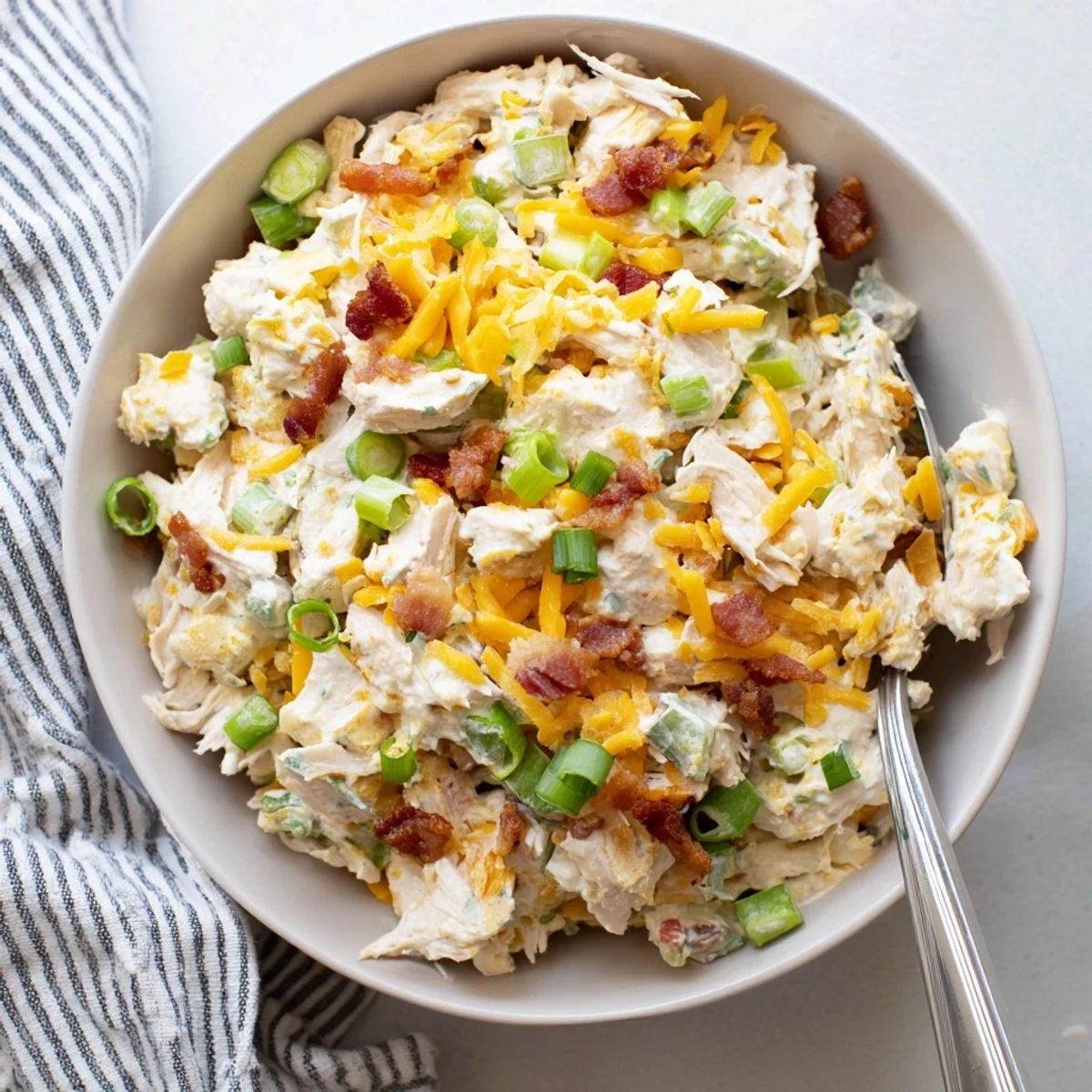 Creamy jalapeno popper keto chicken salad topped with crispy bacon crumbles and fresh green onions in a white serving bowl.