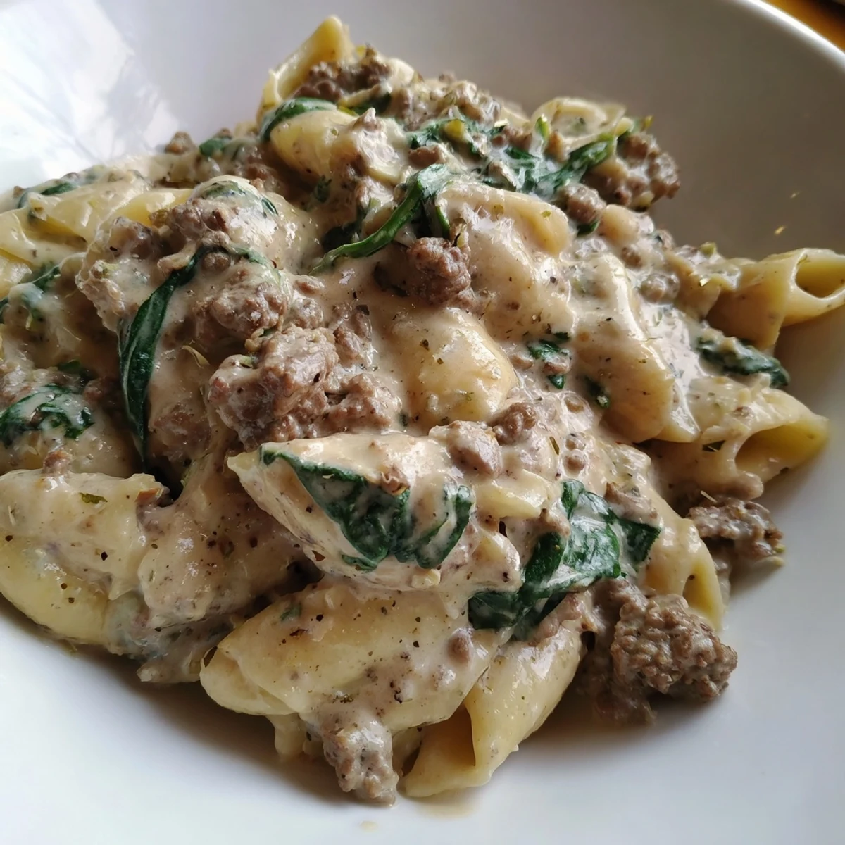 Sizzling skillet of creamy high protein beef pasta with fresh spinach leaves