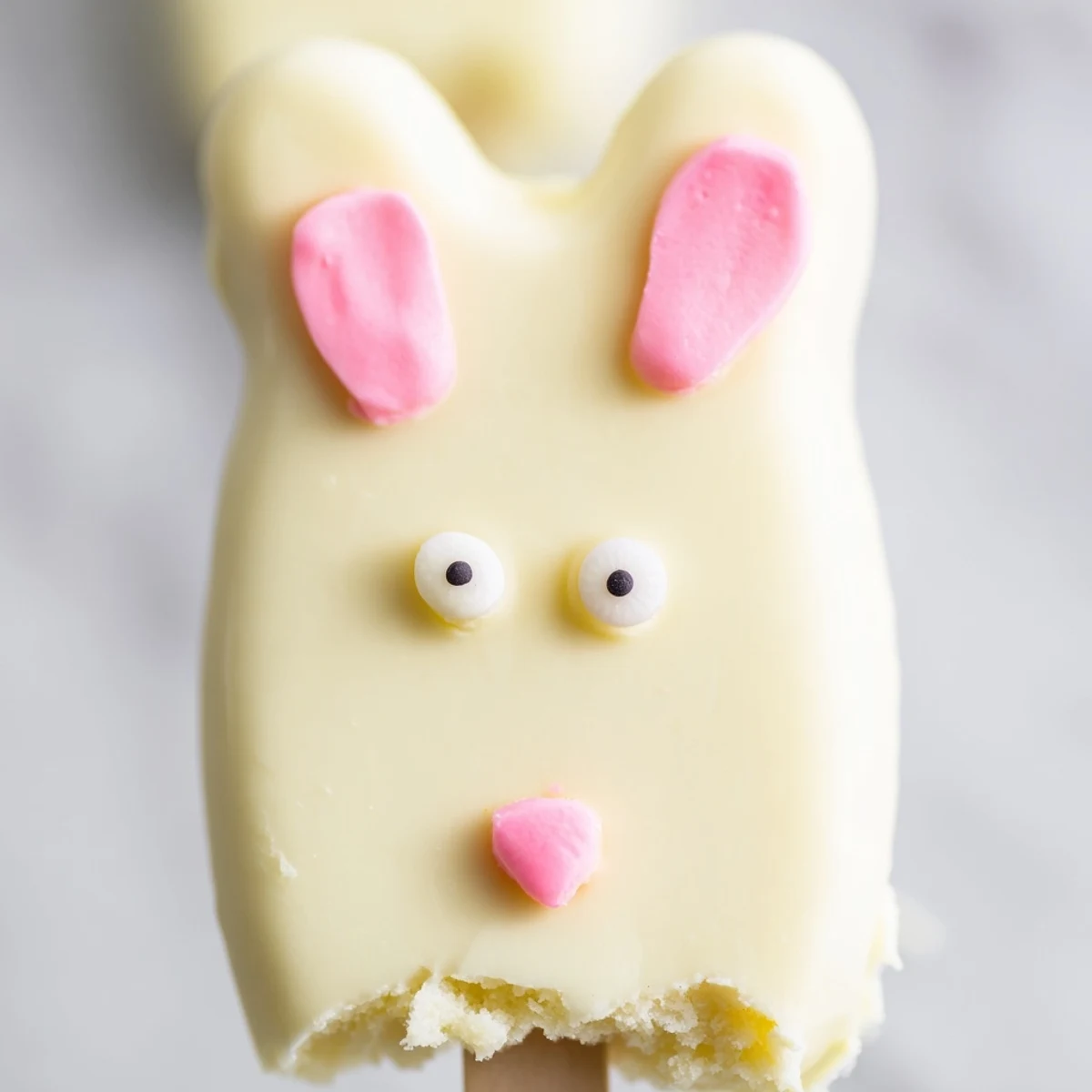 Adorable white chocolate bunny cakesicles with candy eyes on a festive Easter dessert tray