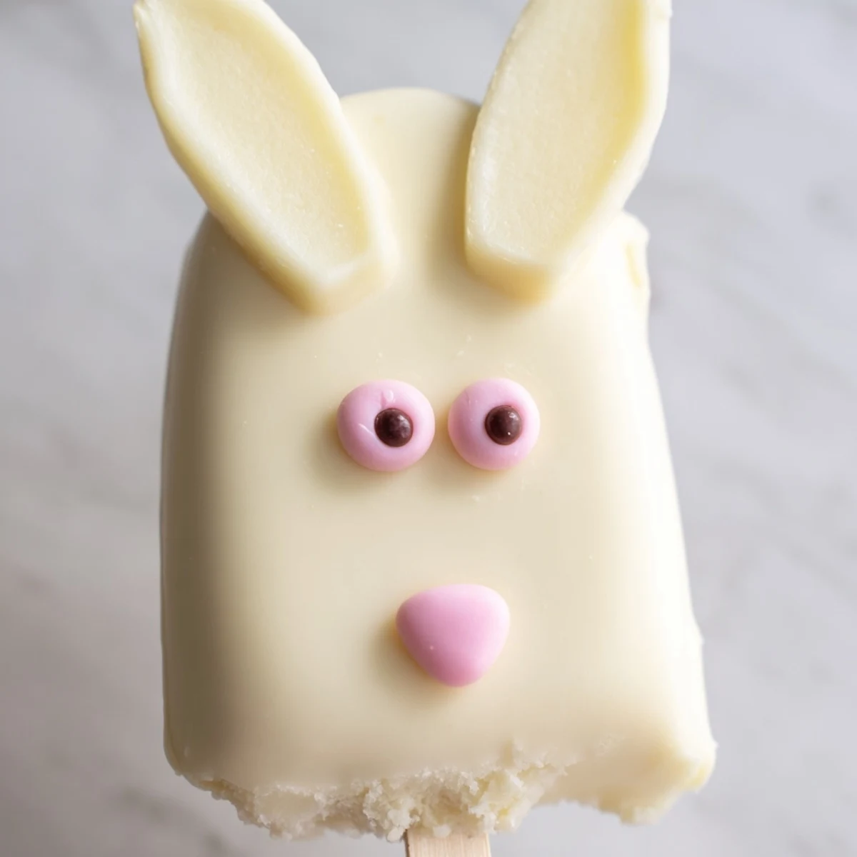 Creamy white chocolate bunny cakesicles decorated with pink ears and colorful spring sprinkles