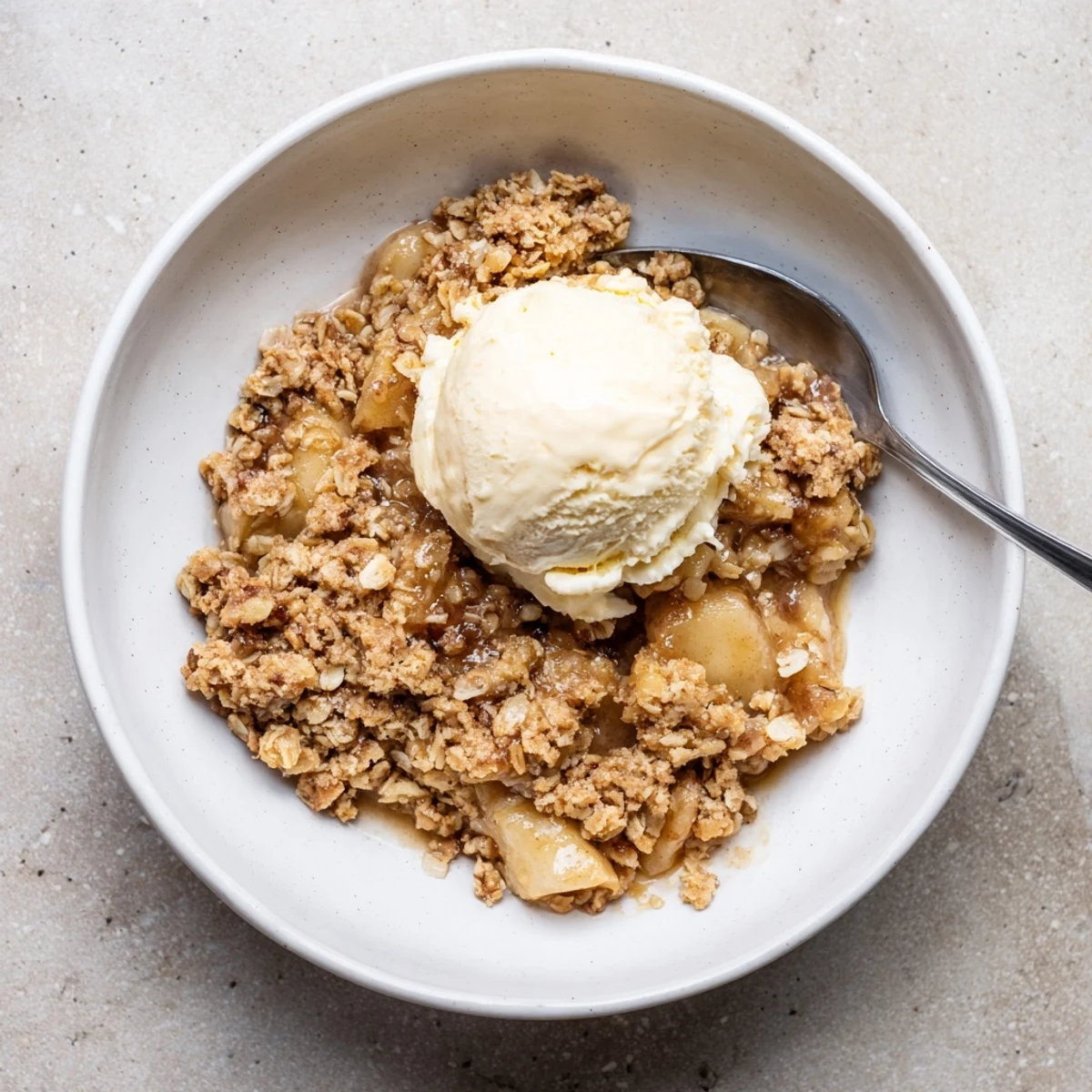 Slow cooker apple crisp served in a white bowl with melty vanilla ice cream