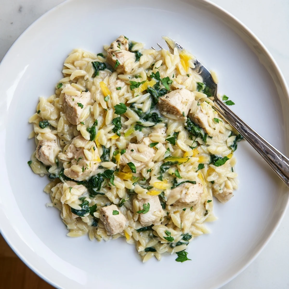 Golden chicken pieces nestled in tender orzo with vibrant spinach and melted pepper jack cheese in a rich garlic sauce