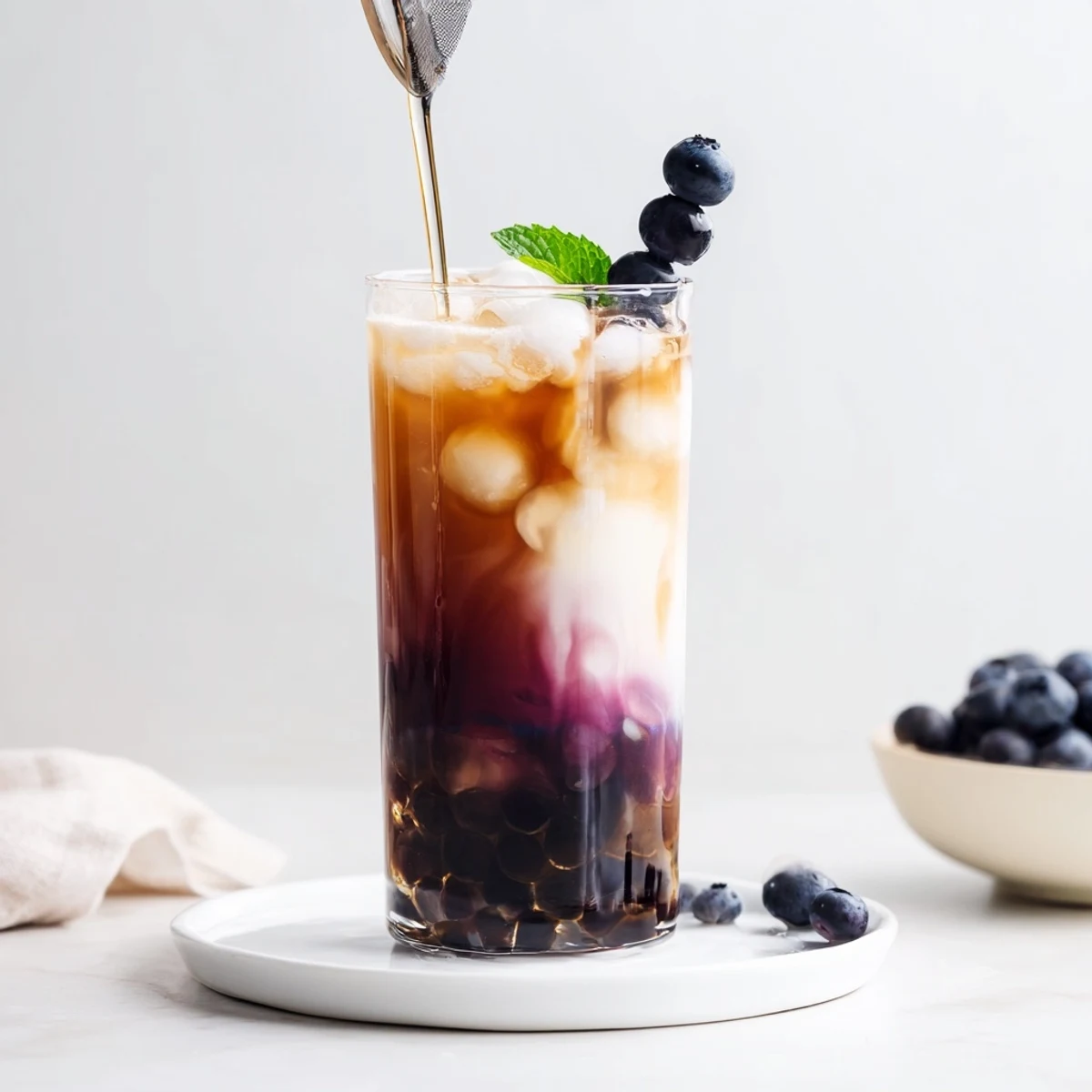 Tall glass of Blueberry Milk Tea Cooler garnished with mint, chewy boba.