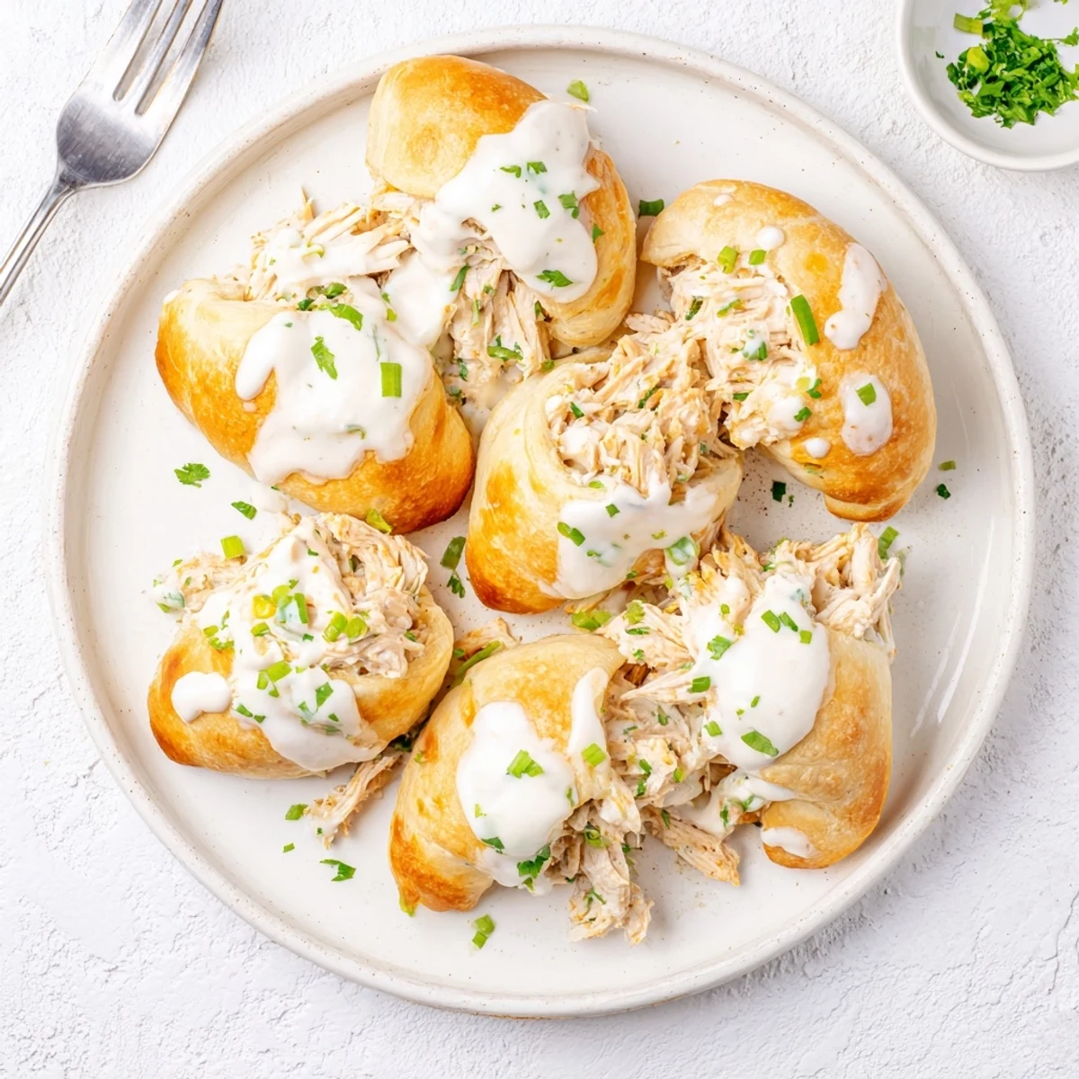 Golden baked chicken pillows with creamy parmesan sauce drizzled over flaky crescent dough