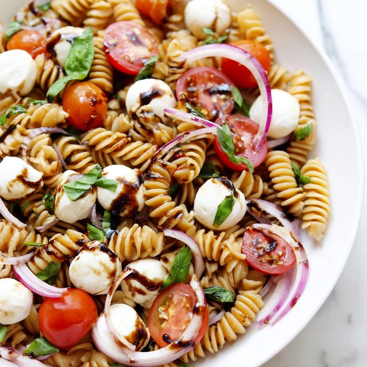 Close-up of Caprese Pasta Salad featuring cherry tomatoes, torn basil, and pearl mozzarella