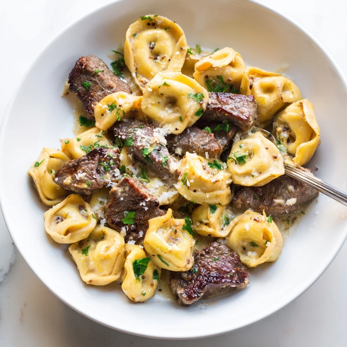 Creamy garlic steak tortellini served in a skillet with melted Parmesan and fresh parsley