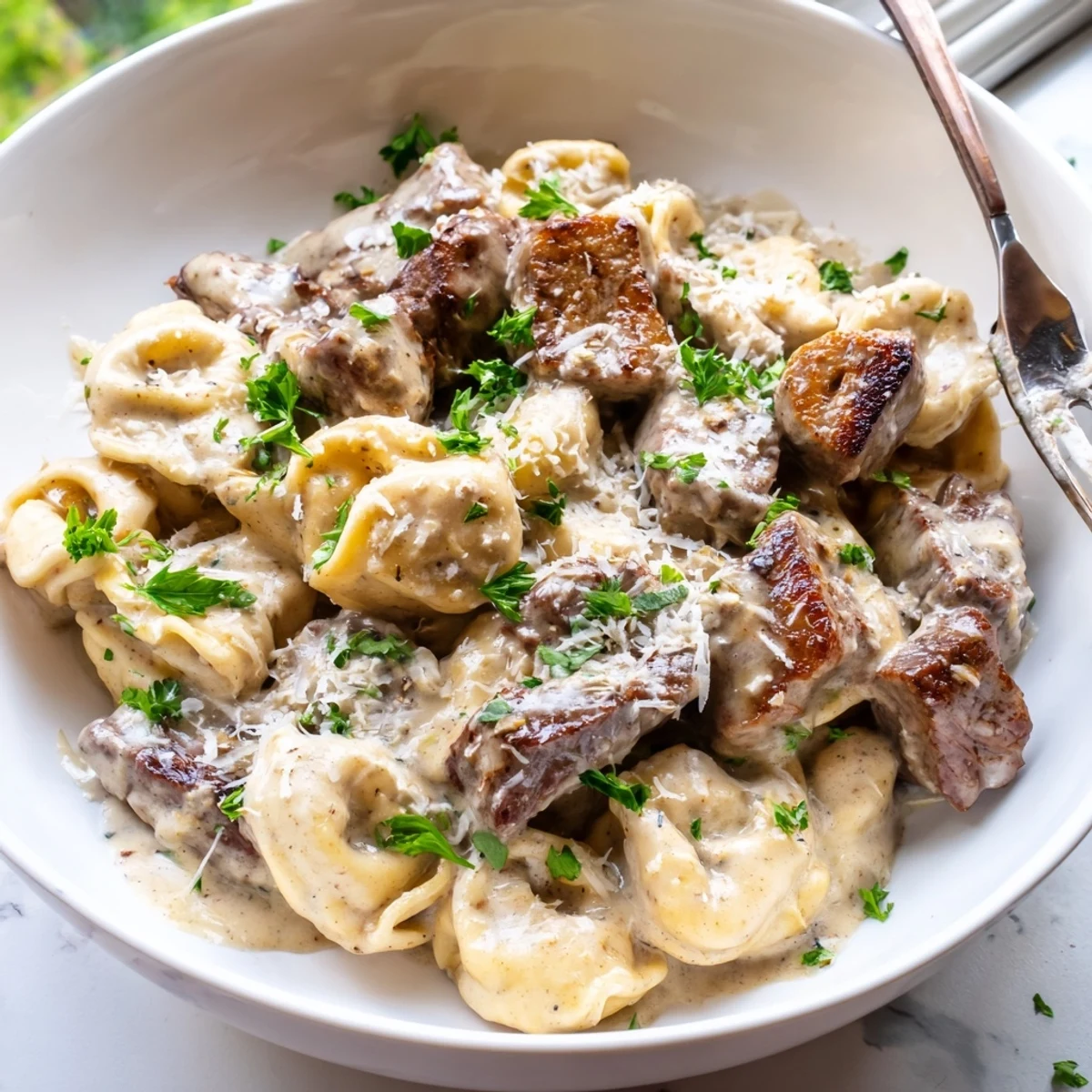Steaming bowl of garlic steak tortellini topped with tender sirloin pieces and fresh chopped parsley