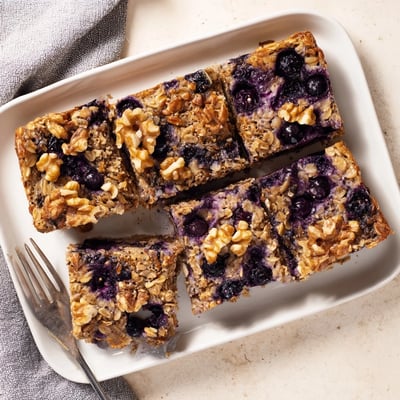 A close slice of High Protein Banana Blueberry Breakfast Bake on a plate, with Greek yogurt and honey.