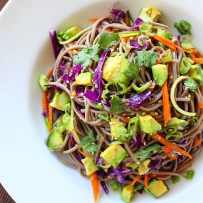 Vibrant Sesame Avocado and Soba Noodle Salad garnished with green onions and sesame seeds in a ceramic bowl.