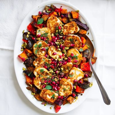 A close-up of Jewelled Haloumi With Spiced Vegetable Bake shows caramelized eggplant and sweet potato with fresh mint and lemon zest garnish.