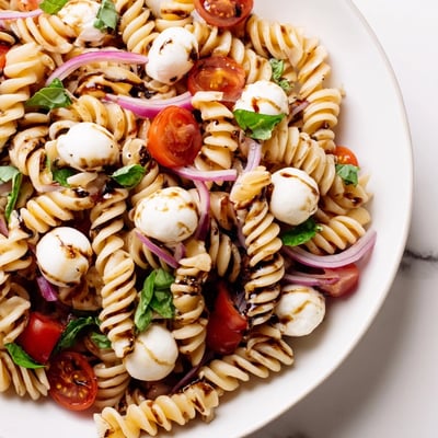 Steaming bowl of Caprese Pasta Salad tossed in a glossy balsamic vinaigrette dressing